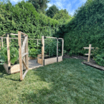 A narrow raised bed garden with fencing and an adjacent raspberry trellis
